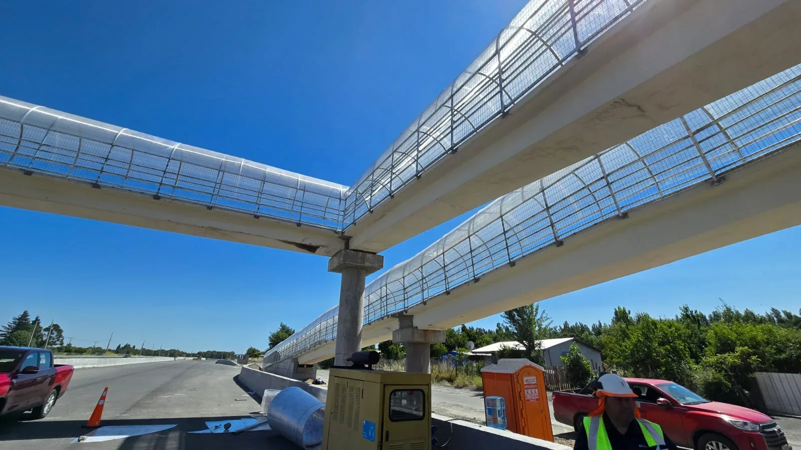 Contrapicado de las dos pasarelas peatonales terminadas cruzando sobre la ruta, con las cúpulas galvanizadas brillando al sol